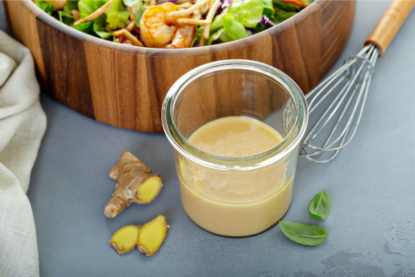 A bowl of creamy dressing, sliced ginger and a large bowl of salad with Asian vegetables